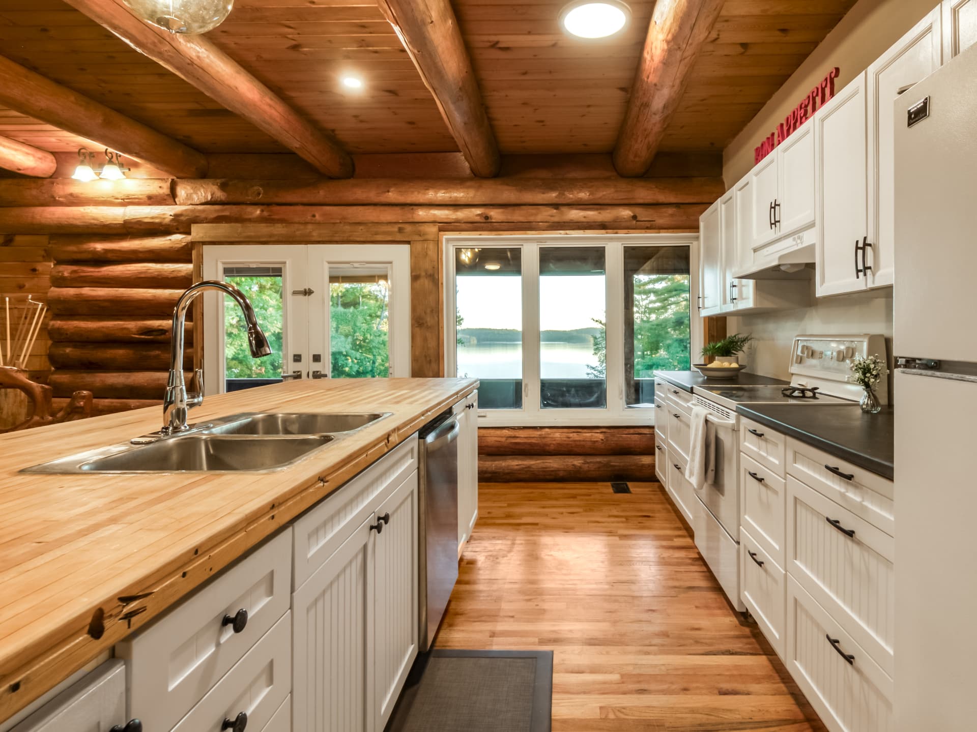 Log-home kitchen with white cabinets and Lake Panache visible through the windows