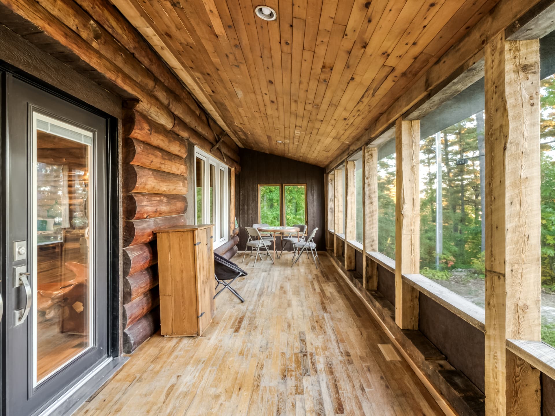 Long screened porch with a table and chairs beside the log home