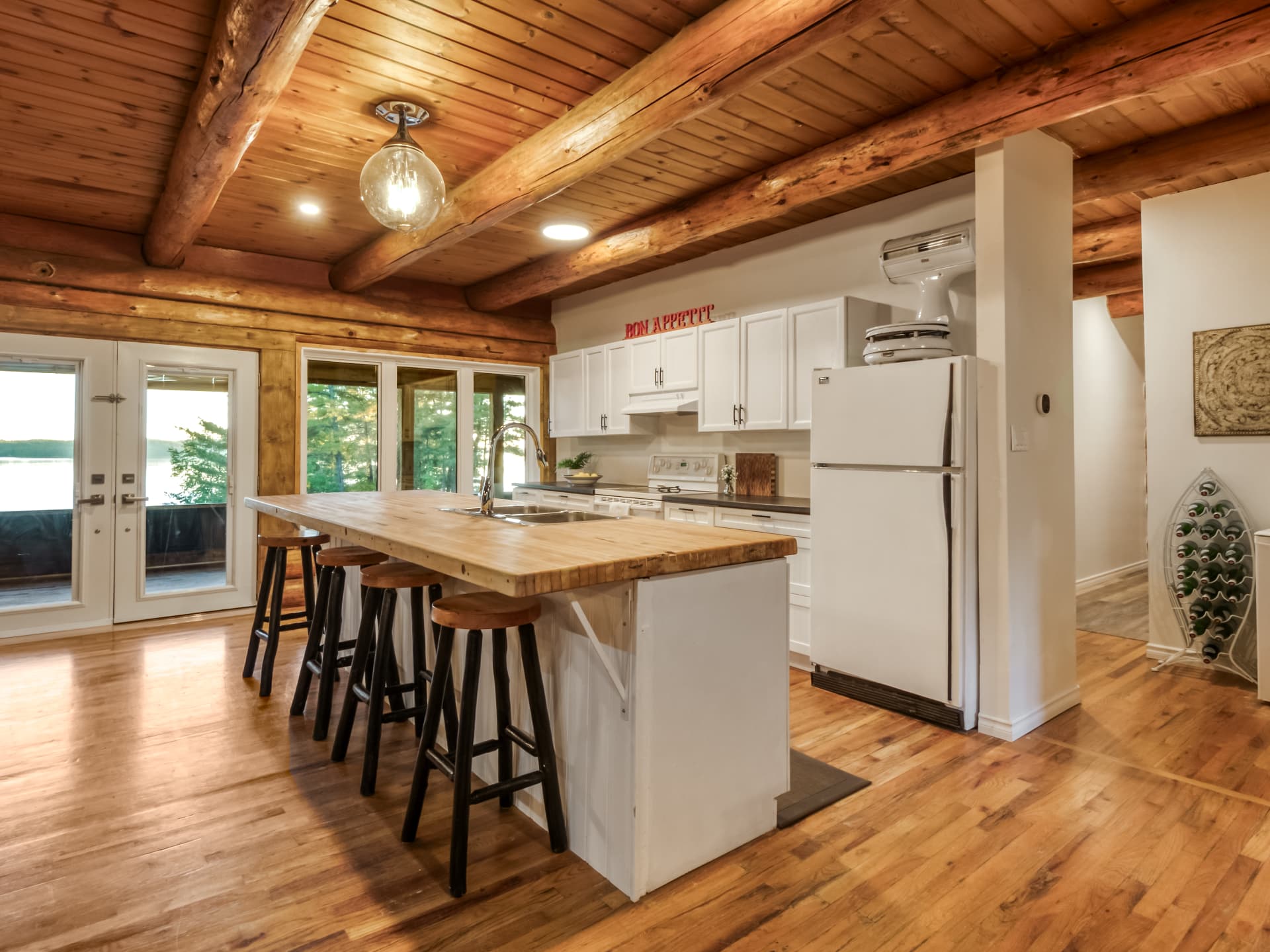Kitchen with a wood island, stools, white cabinetry, and log walls