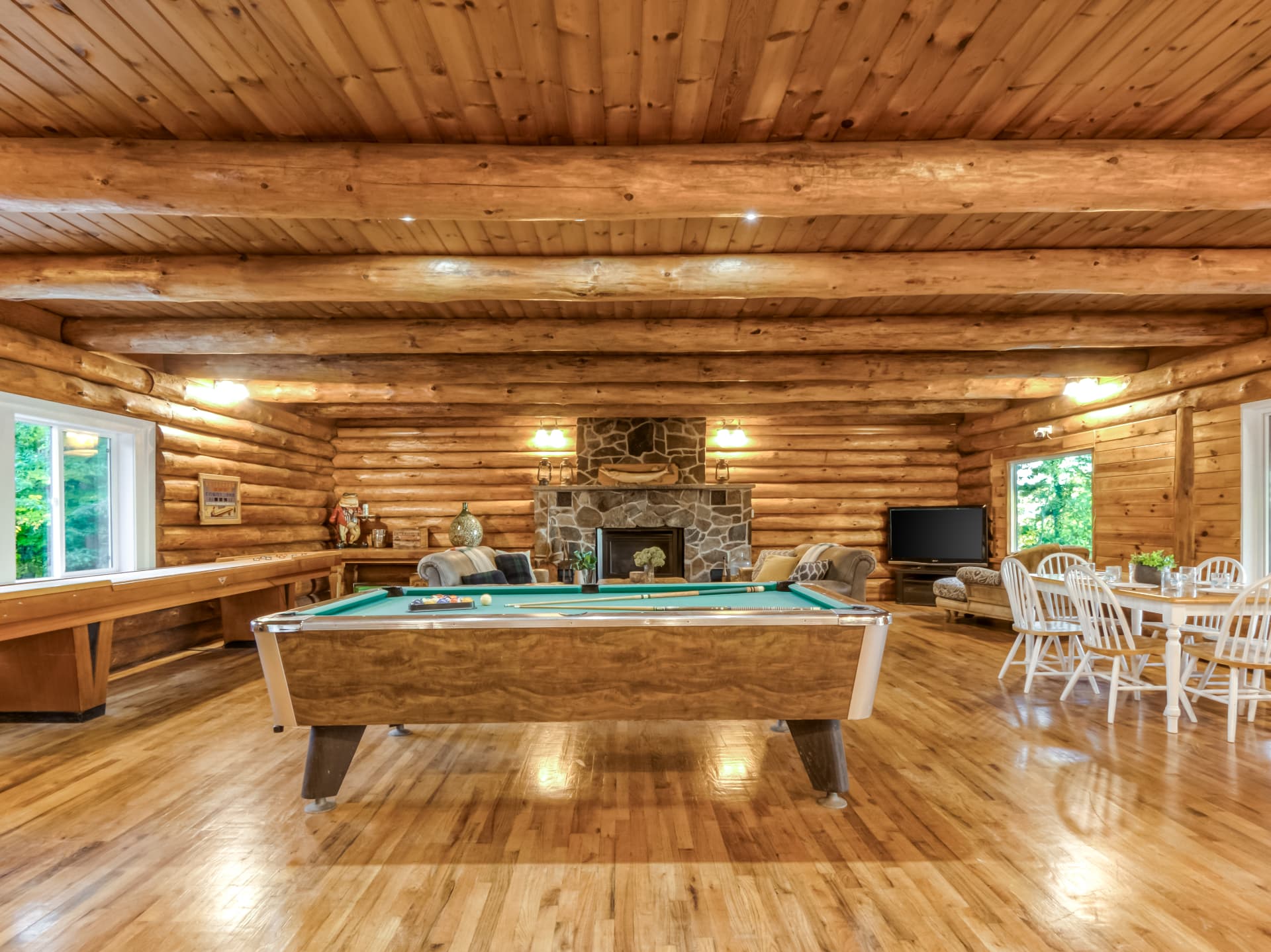 Open-concept log-home living space with a pool table, dining area, and stone fireplace